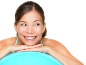 Smiling Eurasian woman leaning on fitness ball