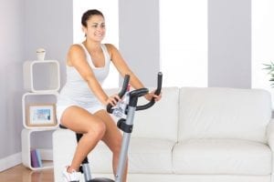 Smiling brunette woman using an exercise bike at home