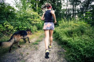 Back view of a fit, young woman walking her dog in the forest