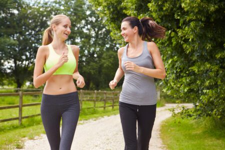 A blonde and brunette woman jogging through a field