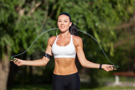 Smiling young brunette woman doing a jump rope exercise outdoors